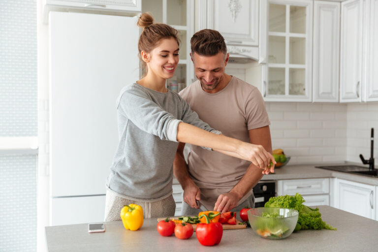 Portrait of a cheerful loving couple cooking salad together
